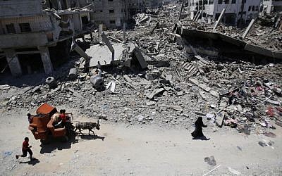 In this August 1, 2014, file photo, Palestinians carry their belongings through the heavily bombed Gaza City neighborhood of Shujaiyah, close to the Israeli border. (AP/Hatem Moussa)
