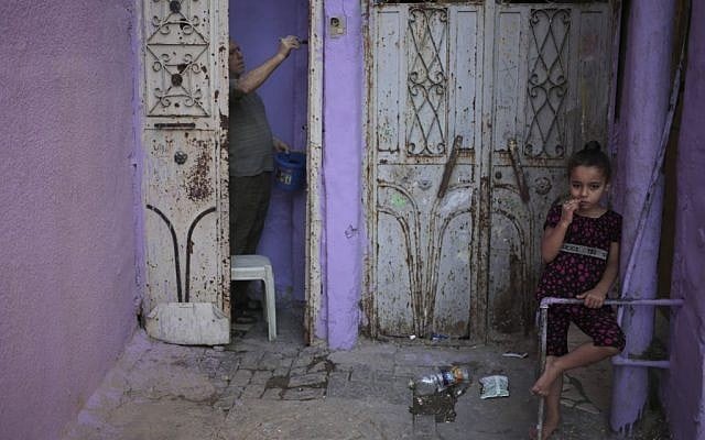 In this June 21, 2015 photo, a Palestinian girl stands on the side while her father paints the door of his house in the old Gaza City. (AP/Khalil Hamra)