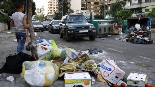 A Syrian boy watches vehicles driving past dumpsters and a pile of garbage in Beirut, Lebanon, Sunday, July 26, 2015 (AP Photo/Hassan Ammar)