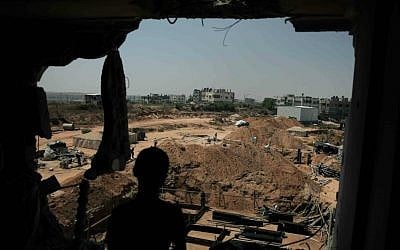 A Palestinian boy looks from his family's destroyed house at workers rebuilding a house which was destroyed during last summer's war between Israel and Hamas, as the long-awaited reconstruction began in the Shejaiya neighborhood of eastern Gaza City on Thursday, July 23, 2015. (AP Photo/Khalil Hamra)