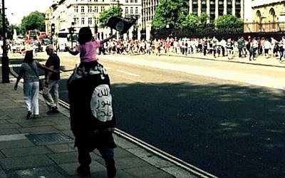 An unidentified man is spotted by tourists walking around London wrapped in an Islamic State flag, carrying a child also waving the flag, July 2015. (Twitter)