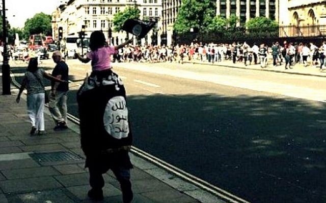 An unidentified man is spotted by tourists walking around London wrapped in an Islamic State flag, carrying a child also waving the flag, July 2015. (Twitter) An unidentified man is spotted by tourists walking around London wrapped in an Islamic State flag, carrying a child also waving the flag, July 2015. (Twitter)