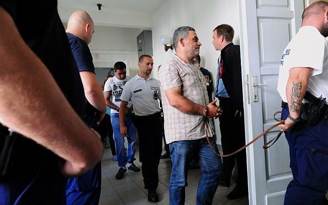 One (C) of four suspects is led by a Hungarian police official into the Kecskemet courtroom on August 29, 2015.  (AFP PHOTO / ATTILA KISBENEDEK)