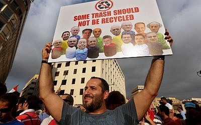 In this August 22, file photo, a Lebanese activist holds a poster with pictures of Lebanese Cabinet ministers during a protest against the ongoing trash crisis, in downtown Beirut, Lebanon. (AP Photo/Bilal Hussein, File)