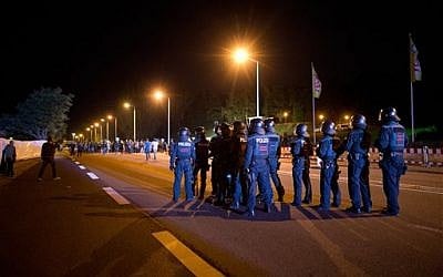 In this Aug. 23, 2015 photo, police secure the street in front of a former DIY market that has been converted into an asylum seeker home as leftist demonstrators gather nearby in Heidenau, south of Dresden, eastern Germany. (Arno Burgi/dpa via AP)