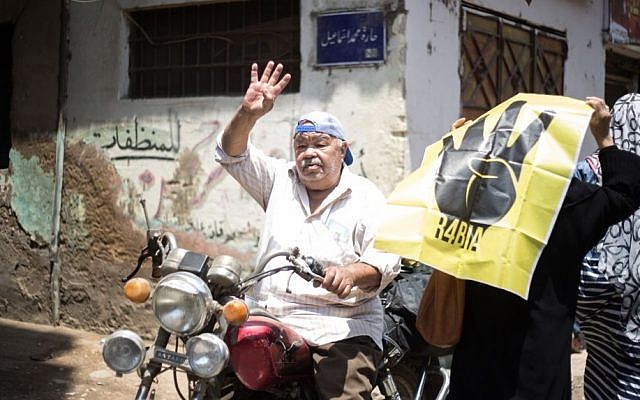 In this Friday, June 7, 2015 photo, a passerby holds up the four-fingered gesture signifying support for Muslim Brotherhood protesters killed by Egyptian security forces outside the Rabaah al-Adawiya mosque in 2013, in the Cairo district of Matariya, Egypt. (AP Photo/Belal Darder) 