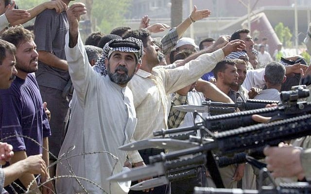 In this June 18, 2003 file photo, US soldiers, partly seen at right, prevent former Iraqi soldiers from trying to enter the American headquarters during a deadly demonstration in Baghdad. (AP Photo/Victor R. Caivano, File)
