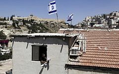 A man looks out of a window of building where Israeli flags fly from the roof, in the Silwan neighborhood of East Jerusalem on August 27, 2015. (AP Photo/Mahmoud Illean)