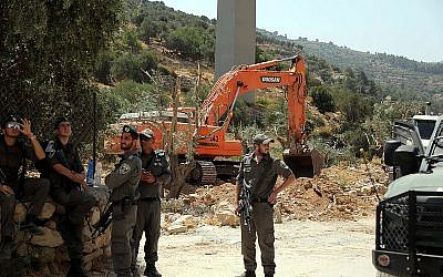 Israeli security forces stand guard as an Israeli excavator uproots olive trees to make way for the separation barrier, in the West Bank town of Beit Jala near the Jewish neighborhood of Gilo and the Palestinian town of Bethlehem on August 17, 2015. (Flash90)