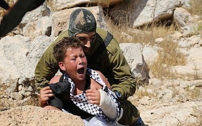 An IDF soldier tries to arrest a 12-year-old boy, accused of stone throwing, at a demonstration in the West Bank village of Nabi Saleh on August 28, 2015 (Eric Cortellessa/ Times of Israel)