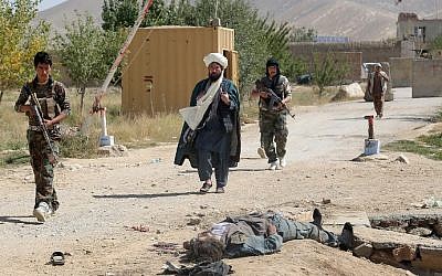 Afghan security forces on guard walk past the body of an alleged Taliban insurgent in military uniform in Ghazni on September 14, 2015.  (Rahmatullah Alizadah/AFP)