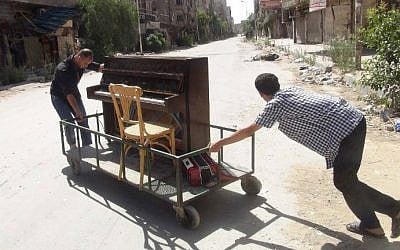 A file picture taken on June 26, 2014 shows Aeham al-Ahmad, a former resident of Damascus's Yarmouk Palestinian refugee camp, being helped by a friend to push his piano along a the street in the southern Damascus suburb. (AFP Photo/Rami Al-Sayed)