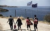 Syrian migrants walk past Greek and European flags as they head towards the town of Mithimna on Lesbos island, after arriving in an inflatable boat from Turkey on August 22, 2015. (AFP PHOTO / ACHILLEAS ZAVALLIS)