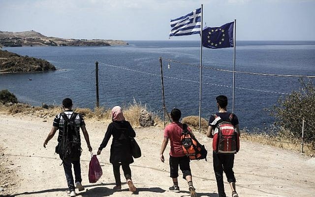Syrian migrants walk past Greek and European flags as they head towards the town of Mithimna on Lesbos island, after arriving in an inflatable boat from Turkey on August 22, 2015. (AFP PHOTO / ACHILLEAS ZAVALLIS) Syrian migrants walk past Greek and European flags as they head towards the town of Mithimna on Lesbos island, after arriving in an inflatable boat from Turkey on August 22, 2015. (AFP PHOTO / ACHILLEAS ZAVALLIS)