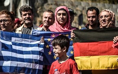 A young migrant stands in front of European Union (C) ,Greek (L) and German (R) flags as migrants and refugees stage a demonstration at Istanbul's Esenler Bus Terminal on September 19, 2015 after authorities withheld tickets to Turkish border towns. Hundreds of refugees camped out at the main bus station in Istanbul for a fifth night running after being refused tickets for Edirne, some 250 kilometres (150 miles) away. Many of the refugees seeking to leave Turkey have been living in the country for months, sometimes years, after fleeing the bloody civil war in neighbouring Syria. AFP PHOTO / OZAN KOSE