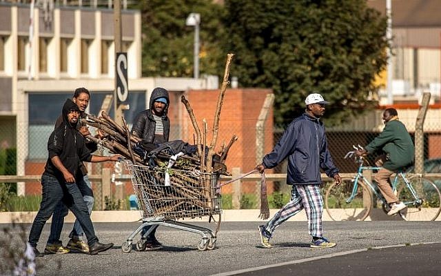 Migrants transport firewood in a trolley at a site dubbed the "New Jungle", where some 3,000 people have set up camp -- most seeking desperately to get to England, in Calais on September 19, 2015. The slum-like migrant camp sprung up after the closure of notorious Red Cross camp Sangatte in 2002, which had become overcrowded and prone to violent riots. However migrants and refugees have kept coming and the "New Jungle" has swelled along with the numbers of those making often deadly attempts to smuggle themselves across the Channel. AFP PHOTO / PHILIPPE HUGUEN