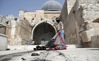 A masked Palestinian wearing a Hamas headband takes a burnt carpet out of Al-Aqsa mosque in Jerusalem's Old City during clashes at the compound on September 13, 2015, just hours before the start of the Jewish new year. (AFP PHOTO/AHMAD GHARABLI)