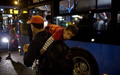 A man carries a child as they try to board a bus provided by Hungarian authorities for migrants and refugees at Keleti train station in Budapest, Hungary, Saturday, Sept. 5, 2015. Hundreds of migrants boarded buses provided by Hungary's government as Austria in the early-morning hours said it and Germany would let them in. (AP Photo/Marko Drobnjakovic)