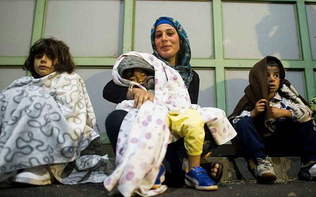 A migrant woman with a sleeping child on her lap smiles after arriving at the border station between Hegyeshalom, Hungary, and Nickelsdorf, Austria, Saturday morning Sept. 5, 2015. (AP Photo/Christian Bruna)