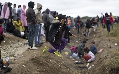 A child jumps over a ditch as people wait in order to clear a police line after entering Croatia from Serbia in Strosinci, Croatia, Saturday, Sept. 26, 2015 (AP Photo/Marko Drobnjakovic)