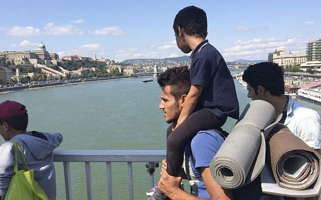 A man carries a boy on his shoulders as a group of hundreds of migrants crossed the river Danube in Budapest, Sept, 4, 2015, after they decided to walk toward Austria. (AP Photo/Bela Szandelszky) A man carries a boy on his shoulders as a group of hundreds of migrants crossed the river Danube in Budapest, Sept, 4, 2015, after they decided to walk toward Austria. (AP Photo/Bela Szandelszky)