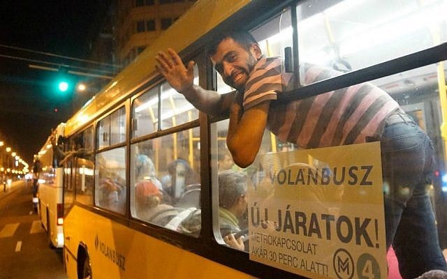 A migrant waves from the window of a bus of Volanbusz company at Keleti Railway Station in Budapest, Hungary, early Saturday, Sept. 5, 2015, after the Hungarian government provided buses to carry about 4,500 migrants to the Hungarian-Austrian border. (Zoltan Balogh/MTI via AP)