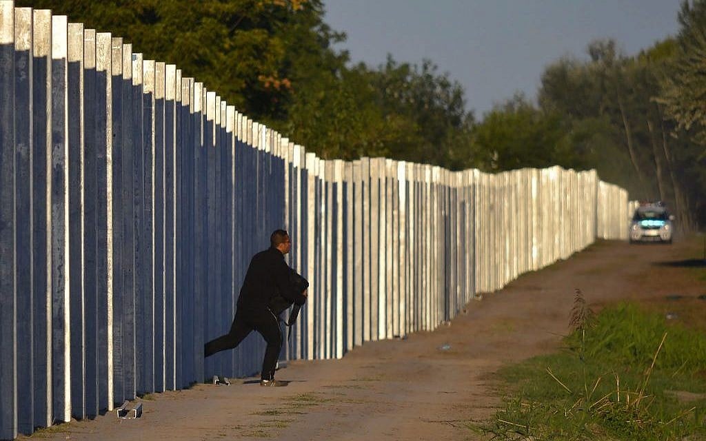 A migrant runs after he enters Hungary by crossing the temporary protection fence along the Hungarian-Serbian border as a police car approaches at Roszke, 180 kms southeast of Budapest, Hungary, Monday, September 7, 2015. (Edvard Molnar/MTI via AP)