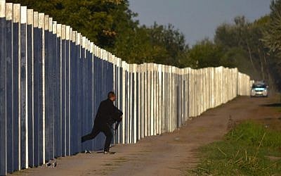 A migrant runs after he enters Hungary by crossing the temporary protection fence along the Hungarian-Serbian border as a police car approaches at Roszke, 180 kms southeast of Budapest, Hungary, Monday, September 7, 2015. (Edvard Molnar/MTI via AP)