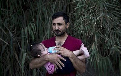 A Syrian refugee feeds milk to his daughter after they arrived on a dinghy, from Turkey to Lesbos island, Greece, Wednesday, Sept. 9, 2015. (AP Photo/Petros Giannakouris)
