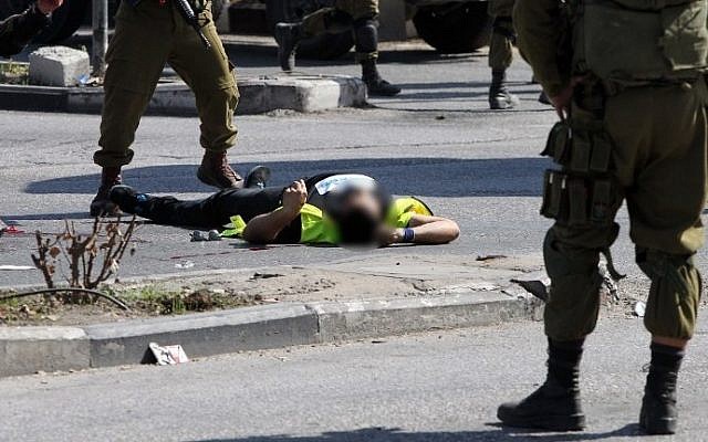 Israeli security forces stand next to the body of a Palestinian man disguised as a news photographer who carried out a stabbing attack against a soldier at the entrance to the city of Hebron on October 16, 2015 (Hazem Bader/AFP) Israeli security forces stand next to the body of a Palestinian man disguised as a news photographer who carried out a stabbing attack against a soldier at the entrance to the city of Hebron on October 16, 2015 (Hazem Bader/AFP)