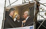 A worker hangs a picture taken by Israeli Government Press Office photographer Avi Ohayon showing former US president Bill Clinton arranging the tie of late Israeli prime minister Yitzhak Rabin along with Rabin's adviser Eitan Haber (L), displayed at an exhibition marking the 20th anniversary of Rabin's assassination, on October 26, 2015 in Tel Aviv. (AFP PHOTO/JACK GUEZ)
