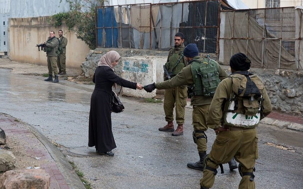 Illustrative: Israeli soldiers check the ID of a Palestinian woman near a Jewish enclave in Hebron on October 29, 2015. (AFP/Menahem Kahana) Illustrative: Israeli soldiers check the ID of a Palestinian woman near a Jewish enclave in Hebron on October 29, 2015. (AFP/Menahem Kahana)