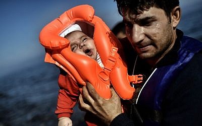 A migrant holds a baby as refugees and migrants arrive at the Greek island of Lesbos after crossing the Aegean sea from Turkey on October 5, 2015. (AFP/ ARIS MESSINIS)