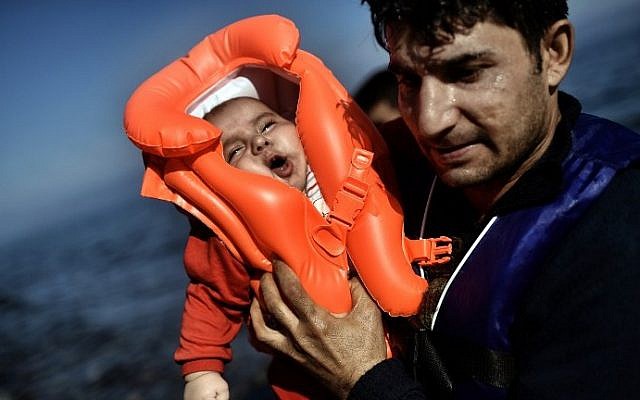 A migrant holds a baby as refugees and migrants arrive at the Greek island of Lesbos after crossing the Aegean sea from Turkey on October 5, 2015. (AFP/ ARIS MESSINIS)