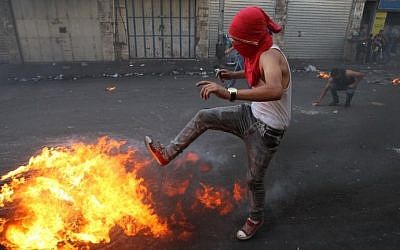 A Palestinian youth kicks a burning tire during clashes with Israeli security forces in the West Bank town of Hebron on October 4, 2015. (AFP/HAZEM BADER) A Palestinian youth kicks a burning tire during clashes with Israeli security forces in the West Bank town of Hebron on October 4, 2015. (AFP/HAZEM BADER)