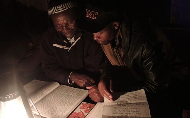 Yosef Njogu, left, and Asher Muiru, who is part of a small community of Jews in the village of Moro, about four hours away, look over a tikkun. A page that fell out of the book when they opened it was a trop [chanting melody] sheet I used for my Bat Mitzvah 17 years ago. (Melanie Lidman/Times of Israel)