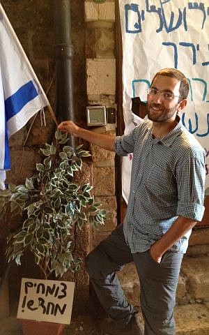 Youth organizer Yair Dan stands next to a tree sapling at the protest tent with a sign reading 'growing anew,' October 8, 2015 (Elhanan Miller/Times of Israel) Youth organizer Yair Dan stands next to a tree sapling at the protest tent, with a sign reading 'growing anew,' October 8, 2015 (Elhanan Miller/Times of Israel)