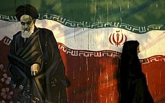 In this November 2, 2013 file photo, a veiled Iranian woman walks past a mural depicting the late revolutionary founder Ayatollah Khomeini, and national Iranian flag, painted on the wall of the former U.S. Embassy, in Tehran, Iran. (AP/Ebrahim Noroozi)