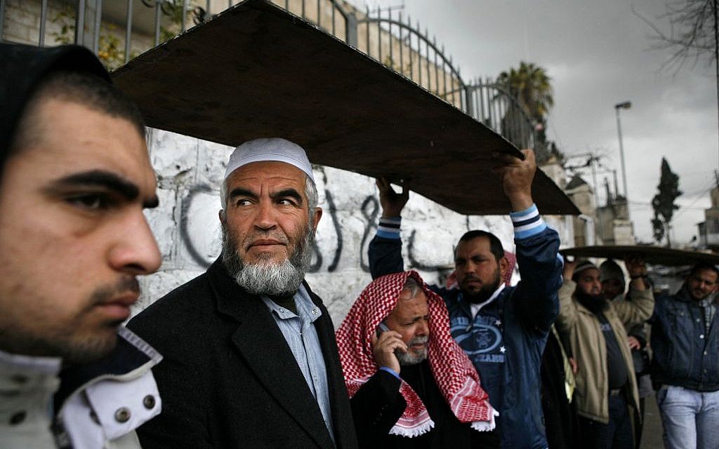 In this Sunday, Feb. 18, 2007 file photo, supporters hold a board to cover from the rain over the head of Sheikh Raed Salah, the leader of the Islamic Movement in Israel, second left, who is prohibited by Israeli court order from entering the The Temple Mount, as he gathers with others outside the Old City in Jerusalem. (AP/Kevin Frayer)
