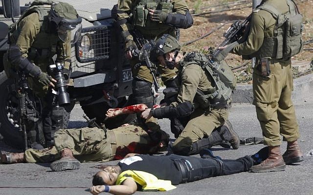 Israeli soldiers treat a wounded comrade after he was stabbed by a Palestinian, seen on the ground, during clashes in Hebron, West Bank Friday, Oct. 16, 2015. The Palestinian man wearing a yellow "press" vest and a T-shirt identifying him as journalist stabbed and wounded an Israeli soldier in the West Bank city of Hebron on Friday before being shot dead by troops, the latest in a month-long spate of attacks. (AP/Nasser Shiyoukhi) Israeli soldiers treat a wounded comrade after he was stabbed by a Palestinian, seen on the ground, during clashes in Hebron, West Bank Friday, Oct. 16, 2015. The Palestinian man wearing a yellow "press" vest and a T-shirt identifying him as journalist stabbed and wounded an Israeli soldier in the West Bank city of Hebron on Friday before being shot dead by troops, the latest in a month-long spate of attacks. (AP/Nasser Shiyoukhi)