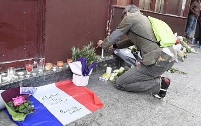 Flowers, candles and the French national flag with Paris's Latin motto 'Tossed but not sunk' written on it, are laid outside next to a Cambodian restaurant a day after 12 people were killed there, on November 14, 2015. (AFP PHOTO/DOMINIQUE FAGET)
