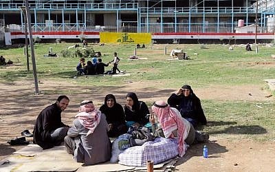 Syrians sit in a park in the capital Damascus, on November 10, 2015. Plastered on the wall in the background are a large version of the Syrian flag and the flag of the Lebanon's Shiite Hezbollah movement. (Louai Beshara/AFP)