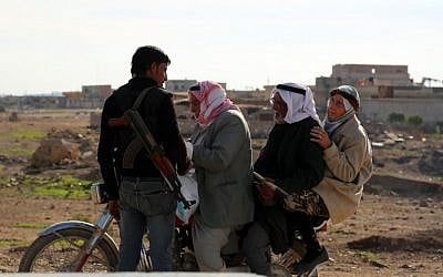 Syrians on a bike stop at a checkpoint monitored by a member of the internal Kurdish security forces in the Al-Shallal suburb of Al-Hol on November 19, 2015, after Syrian Democratic Forces took control of the area from Islamic State. (AFP PHOTO/DELIL SOULEIMAN)