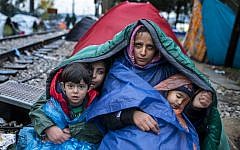 A woman and her children look on as migrants and refugees wait to cross the Greece-Macedonia border in the rain on November 27, 2015 near Gevgelija. (AFP PHOTO / ROBERT ATANASOVSKI)