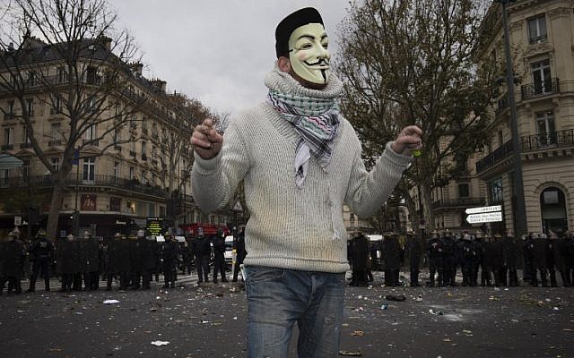 A protester wearing a Guy Fawkes mask stands in front of riot police during clashes following a rally against global warming on November 29, 2015 in Paris, a day ahead of the start of the UN conference on climate change (COP21). (AFP PHOTO / JOEL SAGET / AFP / JOEL SAGET)