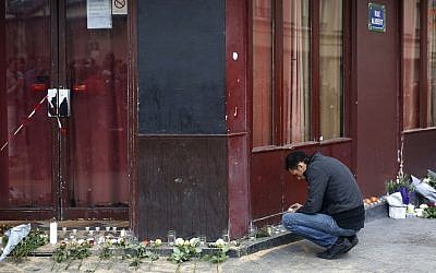 A man places a candle in front of the Carillon cafe in Paris Saturday Nov. 14, 2015, a day after over 120 people were killed in a series of shootings and explosions. (AP Photo/Jerome Delay)