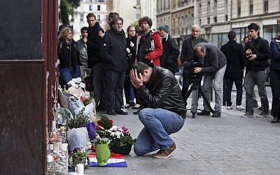 A man holds his head in his hands as he lays flowers in front of the Carillon cafe, in Paris, Saturday, Nov.14, 2015. (AP Photo/Thibault Camus)