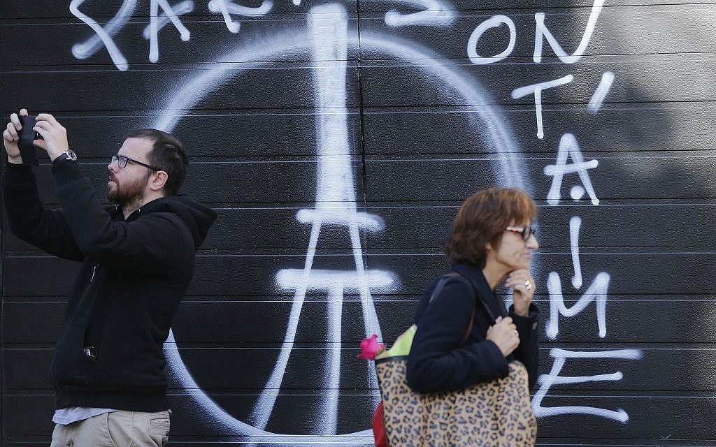 People pass a painting on a garage door opposite the restaurant on Rue de Charonne, Paris, Sunday, Nov. 15, 2015, where attacks took place on Friday. (AP/Frank Augstein)