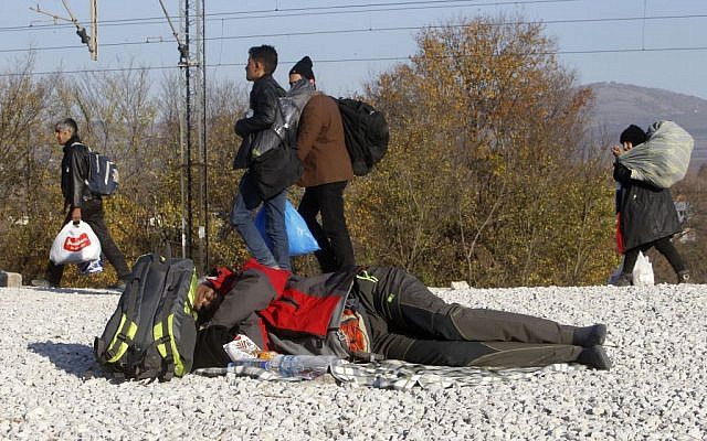 Migrants and refugees walk towards the border with Serbia, while a migrant who was not allowed to cross into Serbia, sleeps on the ground near the village of Tabanovce, in northern Macedonia, November 19, 2015. (AP/Boris Grdanoski) 