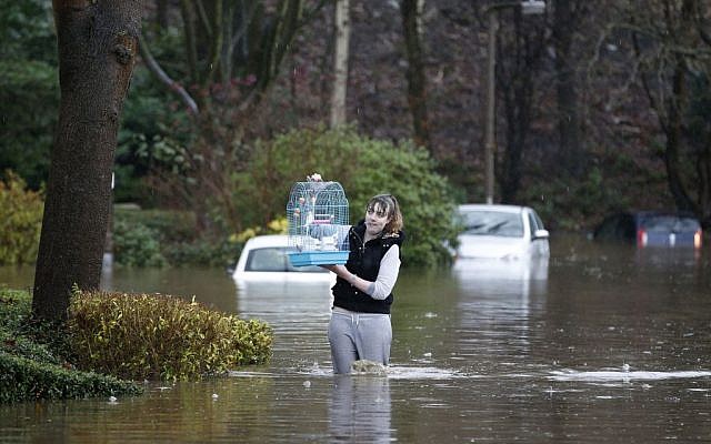 A woman carries a bird cage as she wades through flood water at Mytholmroyd in Calderdale, West Yorkshire, England, Saturday Dec. 26, 2015. (Peter Byrne/PA via AP)